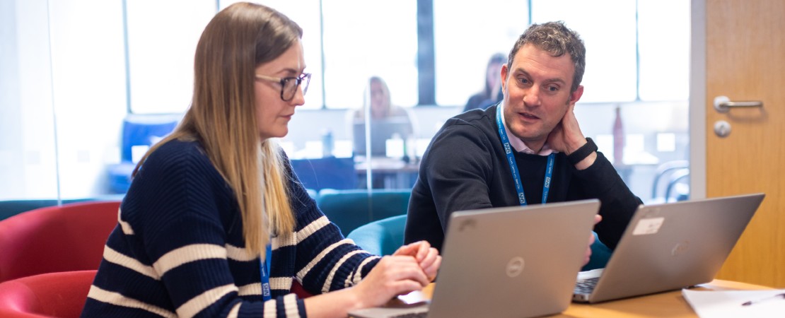 Two members of the transformation consultancy team talking and looking at laptops