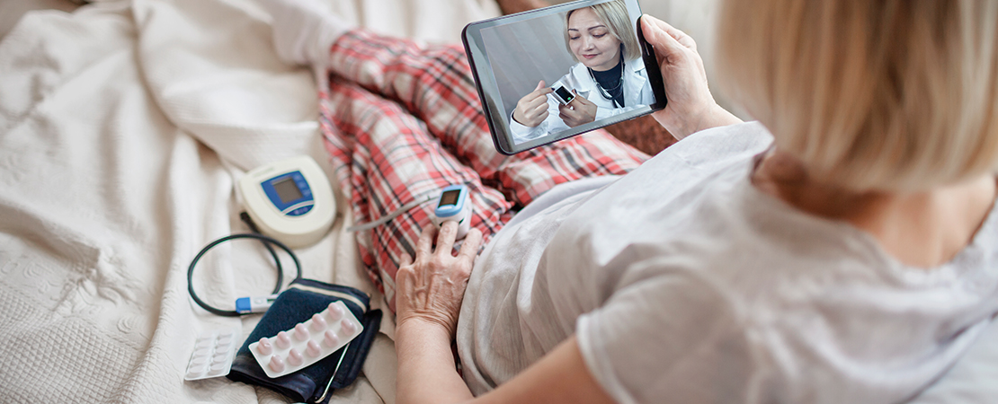 old woman in bed looking at screen and consulting with a doctor online at home