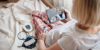 old woman in bed looking at screen and consulting with a doctor online at home